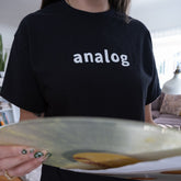 person wearing a black cotton t-shirt with the word analog on it